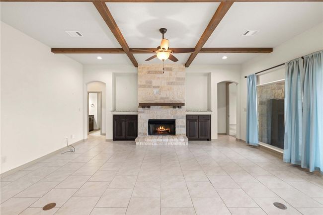 Unfurnished living room featuring visible vents, baseboards, ceiling fan, beamed ceiling, and a fireplace | Image 10