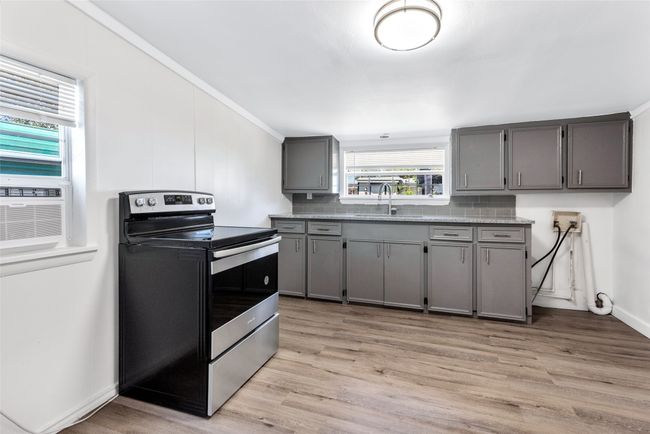 Kitchen with stainless steel electric stove, gray cabinetry, light wood-style flooring, and backsplash | Image 22