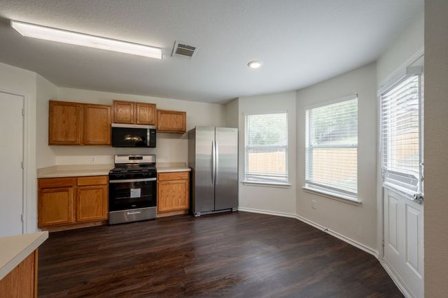 Kitchen with appliances with stainless steel finishes, brown cabinets, dark wood-style flooring, light countertops, and recessed lighting | Image 11