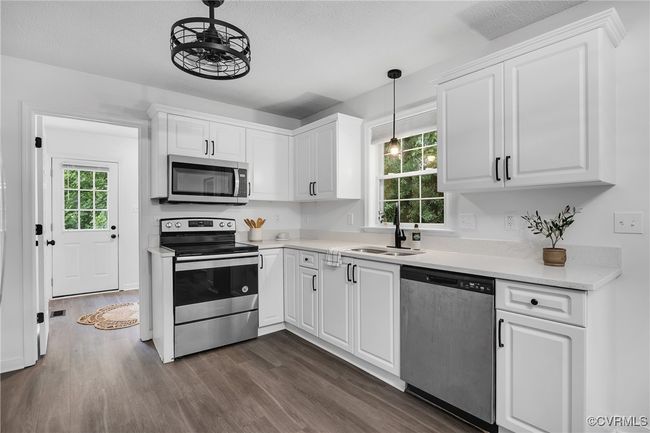 Kitchen featuring appliances with stainless steel finishes, a sink, dark wood-style floors, white cabinets, and light countertops | Image 6