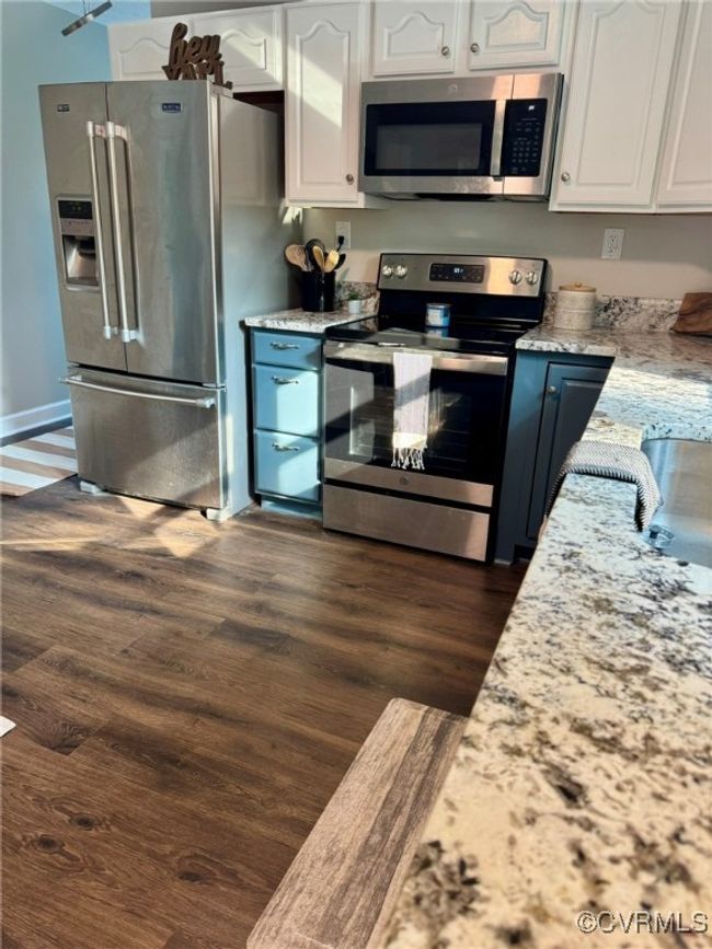 Kitchen with stainless steel appliances, white cabinets, dark wood finished floors, and light stone counters | Image 8