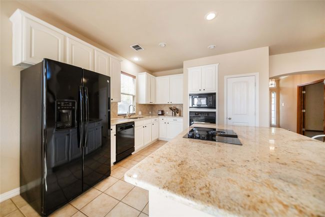 Kitchen with black appliances, arched walkways, white cabinets, light stone counters, and light tile patterned floors | Image 13