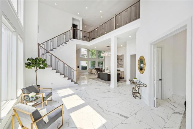 LIVING ROOM: Breathtaking foyer/living room immediately sets the tone for this modern masterpiece. The soaring ceilings create an expansive, airy ambiance, making a dramatic first impression. Beneath your feet, pristine white porcelain floors gleam, reflecting the natural light that pours in through the large, strategically placed windows. | Image 4