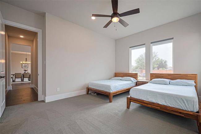 A spacious bedroom with two large windows providing natural light, featuring a ceiling fan. Neutral tones create a calming atmosphere | Image 19
