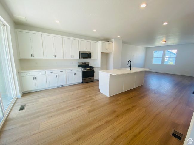 Kitchen with appliances with stainless steel finishes, light wood finished floors, white cabinetry, light countertops, and recessed lighting | Image 6