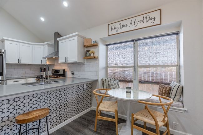 Kitchen featuring wall chimney exhaust hood, wood finished floors, decorative backsplash, white cabinetry, and a sink | Image 14