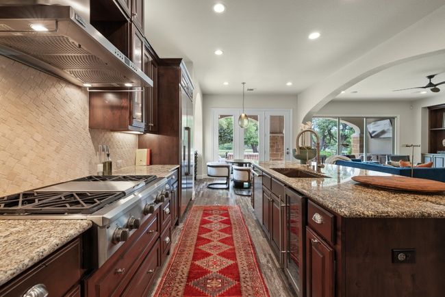Kitchen with wall chimney exhaust hood, a sink, stainless steel gas stovetop, recessed lighting, and arched walkways | Image 13