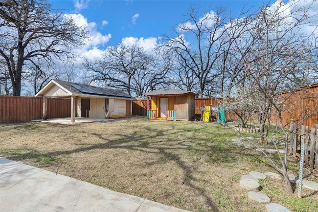 Back of property with a fenced backyard, a shed, an outdoor playhouse structure, solar panels, and covered patio area | Image 16