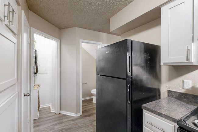 Kitchen with dark countertops, freestanding refrigerator, light wood-style floors, a textured ceiling, and white cabinetry | Image 22