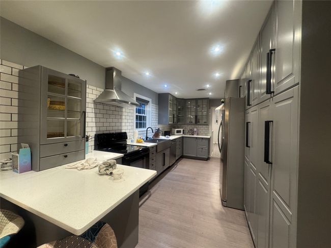 Kitchen featuring wall chimney exhaust hood, a peninsula, freestanding refrigerator, gray cabinets, and tasteful backsplash | Image 5