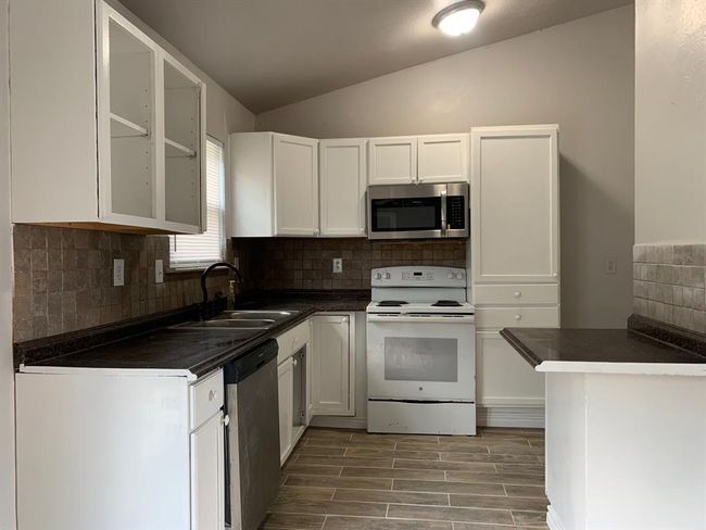 Kitchen featuring white cabinetry, appliances with stainless steel finishes, backsplash, sink, and vaulted ceiling | Image 5