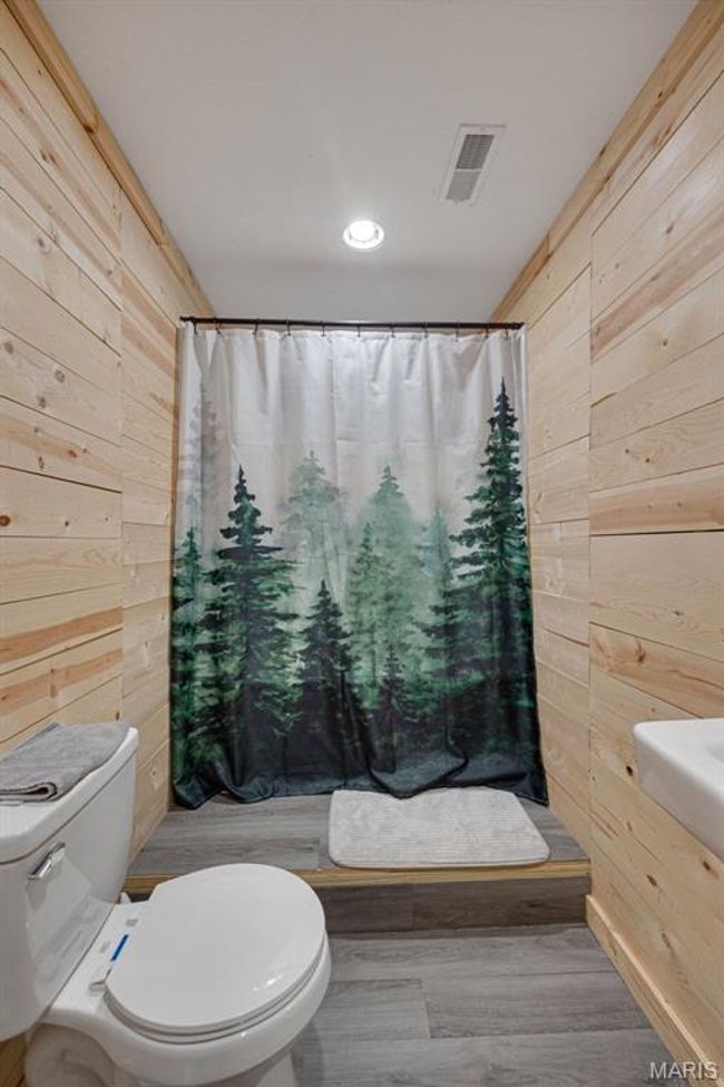 Full bath featuring wooden walls, toilet, curtained shower, and wood finished floors | Image 16
