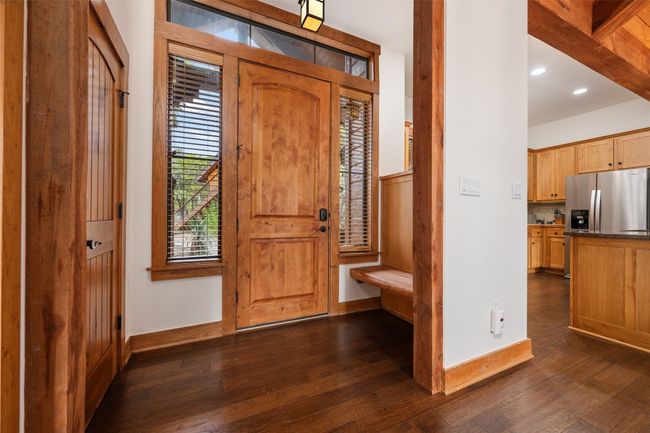 The welcoming entryway features a natural wood door flanked by tall windows, bringing in abundant light. A built-in bench provides a practical seating area. | Image 4