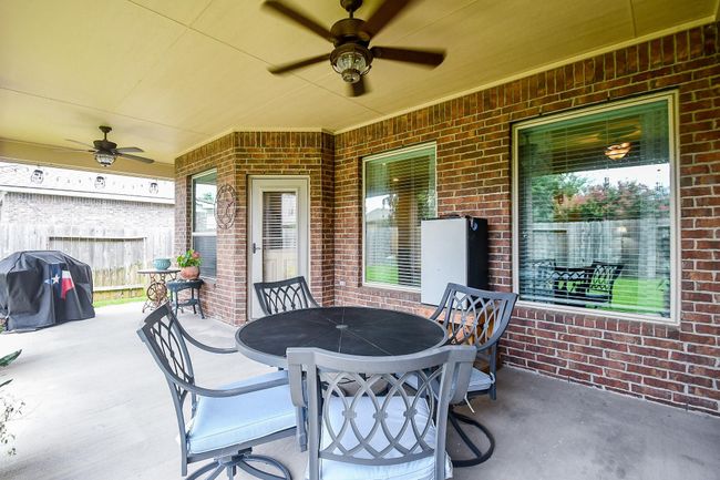 The patio features a covered area with ceiling fans, a round table with cushioned chairs, and a barbecue grill, all set against a brick exterior. | Image 28