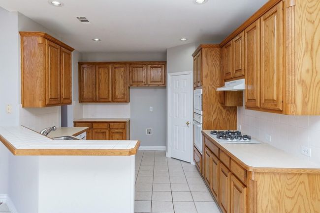 Kitchen with light tile patterned flooring, under cabinet range hood, a peninsula, a sink, and brown cabinets | Image 7