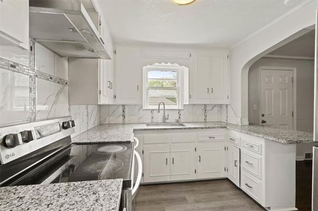 Kitchen featuring stainless steel range with electric cooktop, wall chimney range hood, white cabinets, and crown molding | Image 12