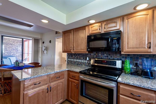 Kitchen featuring stainless steel range with electric cooktop, recessed lighting, light stone counters, black microwave, and a peninsula | Image 5