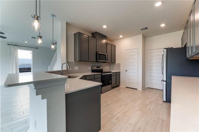 Kitchen with stainless steel appliances, light wood-type flooring, tasteful backsplash, a peninsula, and hanging light fixtures | Image 12