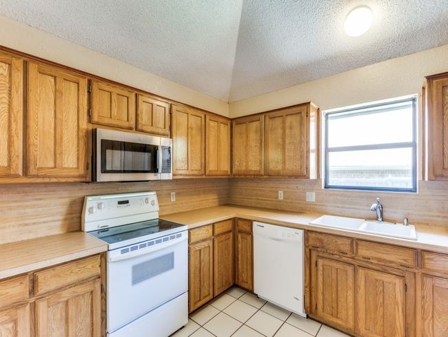 Kitchen with white appliances, light countertops, a textured ceiling, brown cabinets, and light tile patterned floors | Image 13