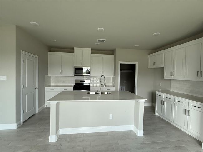 Kitchen featuring stainless steel appliances, tasteful backsplash, white cabinetry, a kitchen island with sink, and light countertops | Image 10