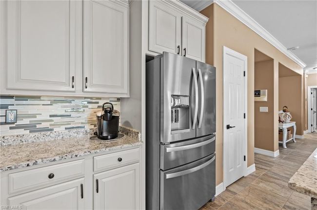 Kitchen featuring stainless steel fridge with ice dispenser, ornamental molding, tasteful backsplash, white cabinetry, and baseboards | Image 21