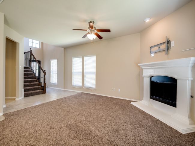 Unfurnished living room featuring a fireplace with raised hearth, light tile patterned floors, light carpet, a ceiling fan, and stairway | Image 4