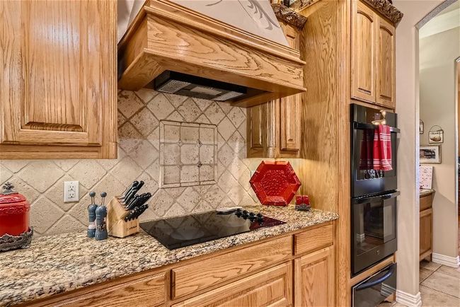 Kitchen with light stone counters, decorative backsplash, custom exhaust hood, black appliances, and a warming drawer | Image 13