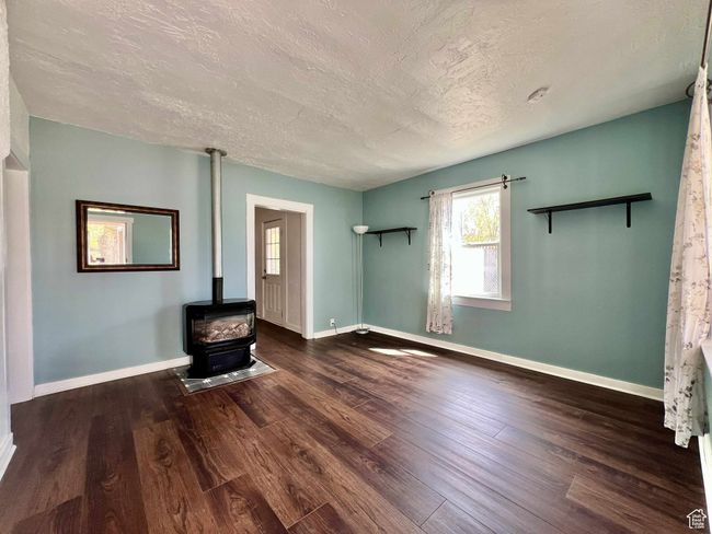 Unfurnished living room featuring baseboards, a wood stove, wood finished floors, and a textured ceiling | Image 7