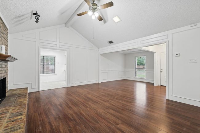 Unfurnished living room with a decorative wall, a ceiling fan, a brick fireplace, dark wood finished floors, and a textured ceiling | Image 6
