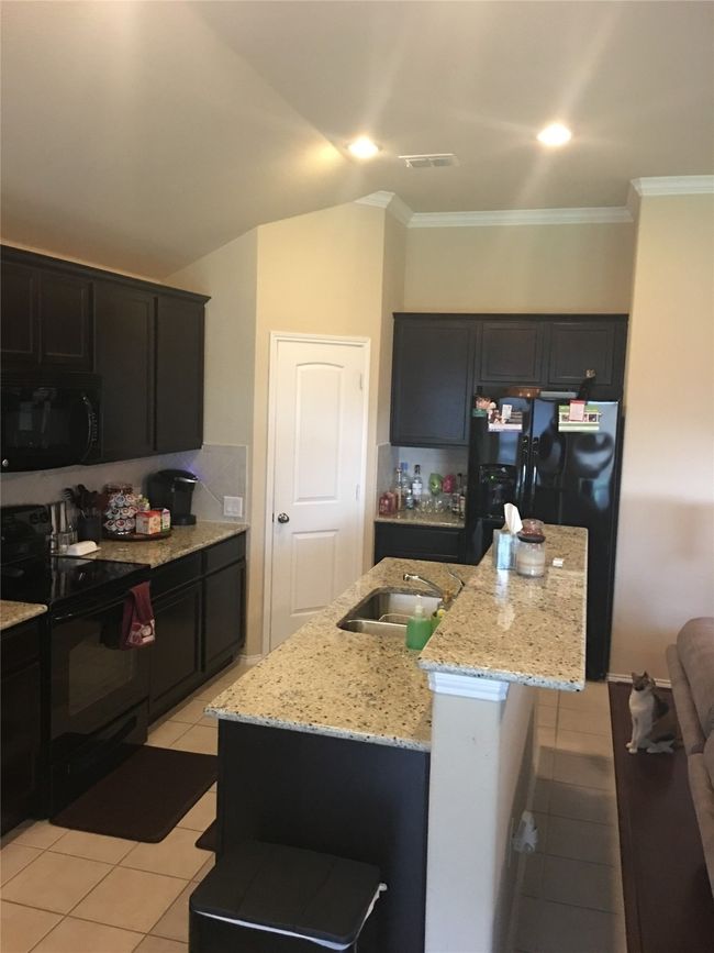 Kitchen featuring black appliances, light tile patterned floors, light stone counters, crown molding, and a sink | Image 9