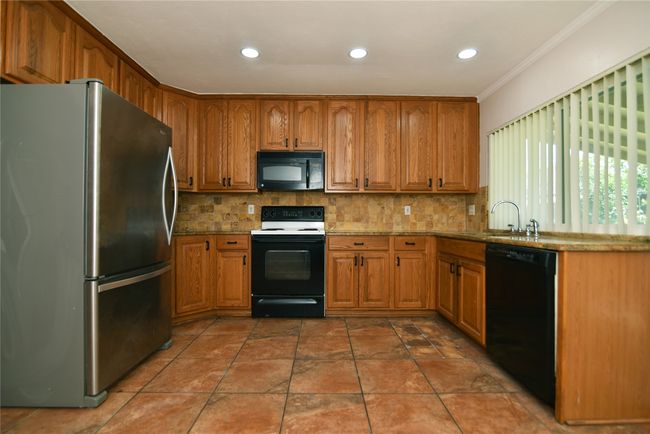Kitchen featuring black appliances, a sink, brown cabinets, ornamental molding, and recessed lighting | Image 11