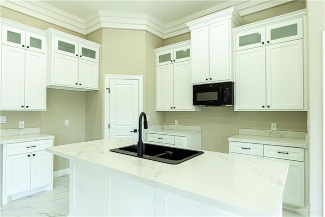 Kitchen with glass insert cabinets, marble finish floor, a kitchen island with sink, black microwave, and a sink | Image 15