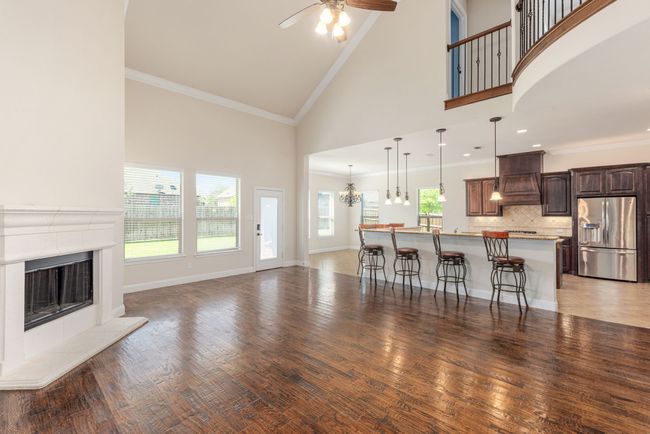 Living area with ceiling fan with notable chandelier, high vaulted ceiling, a fireplace with raised hearth, and crown molding | Image 16