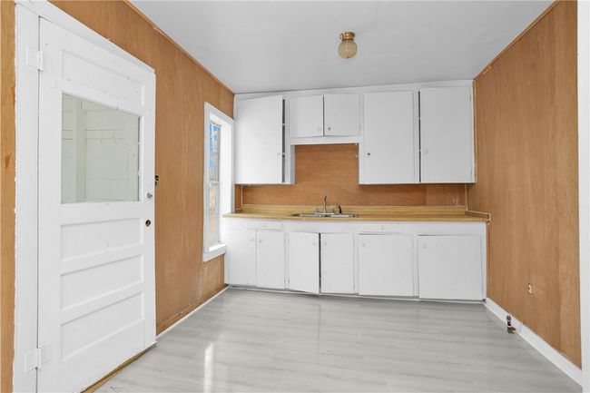 Kitchen with light countertops, white cabinetry, light wood finished floors, and wood walls | Image 19
