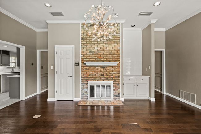 Unfurnished living room featuring crown molding, a chandelier, hardwood / wood-style flooring, a brick fireplace, and recessed lighting | Image 11