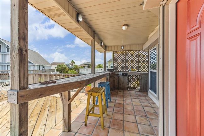 This photo showcases a charming outdoor patio area with rustic wooden countertops and tiled flooring. The space is partially covered, offering a mix of shade and sunlight, with views of neighboring houses and lush greenery. Perfect for entertaining or relaxing. | Image 5