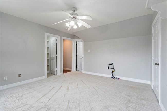 Unfurnished bedroom with carpet floors, baseboards, a walk in closet, a ceiling fan, and lofted ceiling | Image 21