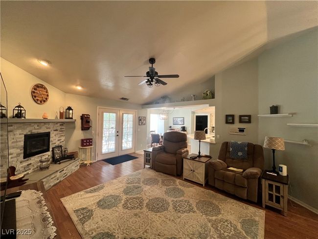 Living room featuring vaulted ceiling, ceiling fan, wood finished floors, french doors, and a stone fireplace | Image 6