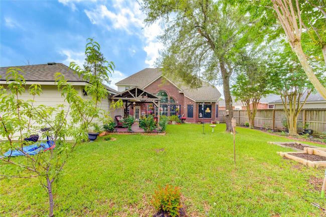 This spacious backyard features a well-maintained lawn, mature trees, and a charming pergola over a patio area, perfect for outdoor relaxation and entertainment. The brick exterior of the house adds a classic touch, with a fenced perimeter offering privacy. | Image 7