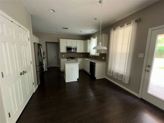 Kitchen with stainless steel appliances, a sink, dark wood-style flooring, a kitchen island, and white cabinetry | Image 10