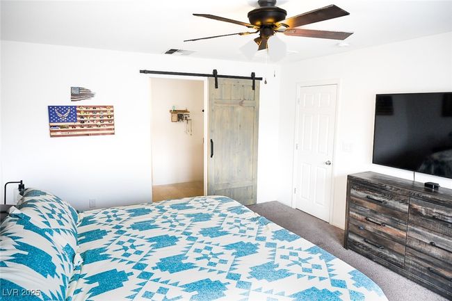 Carpeted bedroom featuring a ceiling fan, visible vents, and a barn door | Image 22