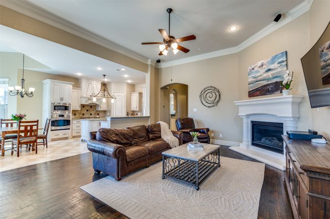Living room with ornamental molding, ceiling fan with notable chandelier, wood finished floors, a glass covered fireplace, and baseboards | Image 11