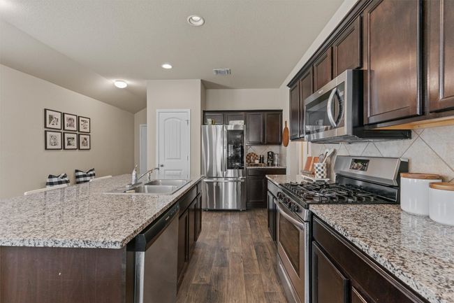 Kitchen with appliances with stainless steel finishes, dark wood-style floors, dark brown cabinetry, backsplash, and a center island with sink | Image 7