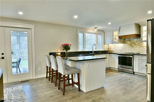 Kitchen with a peninsula, stainless steel range with electric stovetop, visible vents, dark countertops, and premium range hood | Image 15