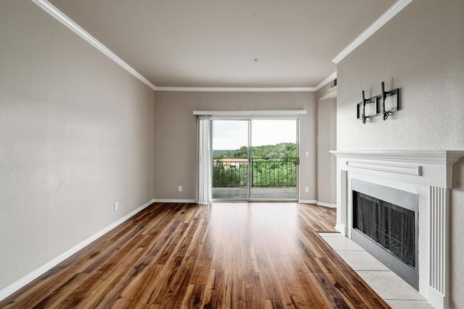 Unfurnished living room with wood finished floors, a fireplace with flush hearth, and ornamental molding | Image 10