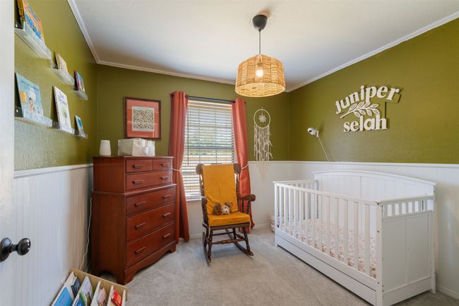 Carpeted bedroom featuring a wainscoted wall, crown molding, and a nursery area | Image 13