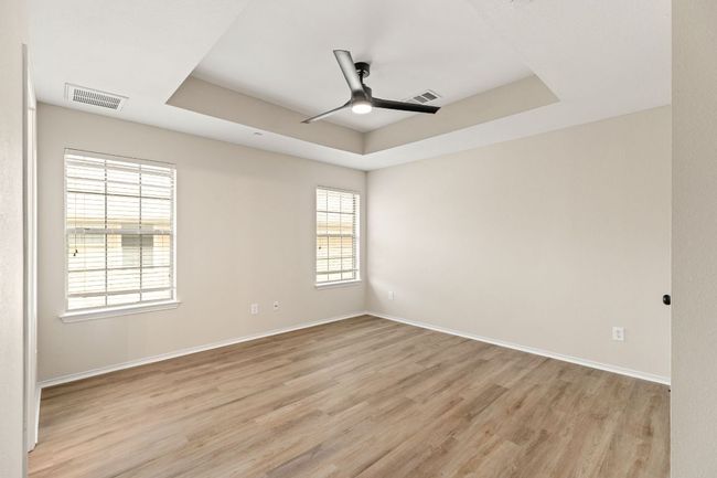 Unfurnished room featuring a ceiling fan, visible vents, light wood-style floors, and a raised ceiling | Image 17