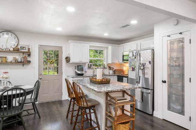 Kitchen featuring appliances with stainless steel finishes, a kitchen breakfast bar, light stone countertops, a kitchen island, and white cabinets | Image 15