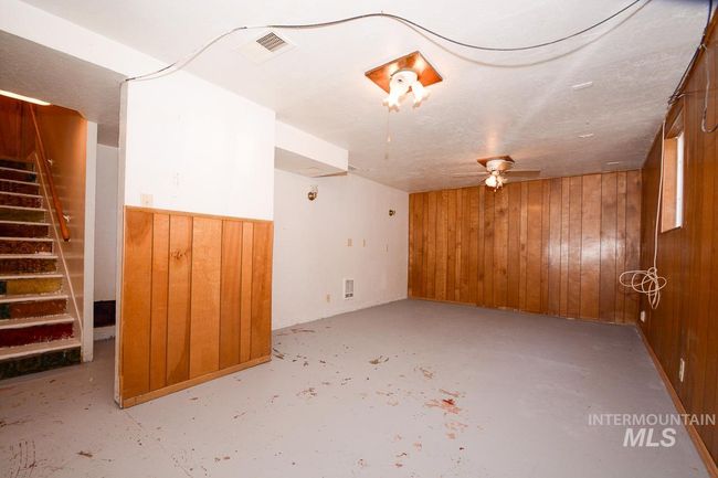 Empty room featuring wood walls, unfinished concrete flooring, stairway, and a ceiling fan | Image 30