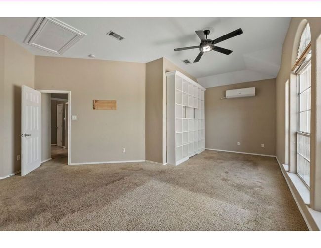Carpeted spare room featuring attic access, vaulted ceiling, a wall unit AC, and ceiling fan | Image 27